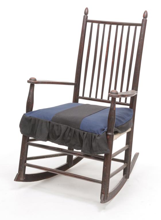 SHAKER ROCKER.: Late 19th century, hardwoods. Old alligatored paint. Turned finials, spindle back, button arms, and wool tape seat in blue and grey. Black and grey cushion. Left arm split at stile. 14.5" seat, 37.5"h