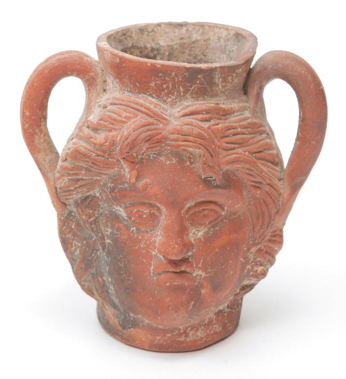 ETRUSCAN FIGURAL TERRACOTTA CUP.: Double handled cup with molded face most likely of a man. Faint scratched letters on the rim. Wear, additional pottery shards inside. 4"h.