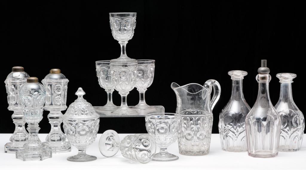 FOURTEEN PIECES OF AMERICAN PATTERN GLASS.: Mid 19th century. Flint glass. Nine are Bull's eye and fleur de lys pattern. Pitcher (chips), 9.25"h., whale oil lamp, 10"h., lidded sugar (chips), 9"h., buttermilk goblet, 5.25"h. and five goblets, 6