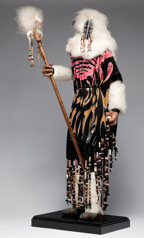 KACHINA BY VERN ROLLIN.: Signed and dated (19)93 on bead. Composition buffalo figure with pottery beads, cloth, leather, fur and original paint, holding a staff. 33"h. including base.