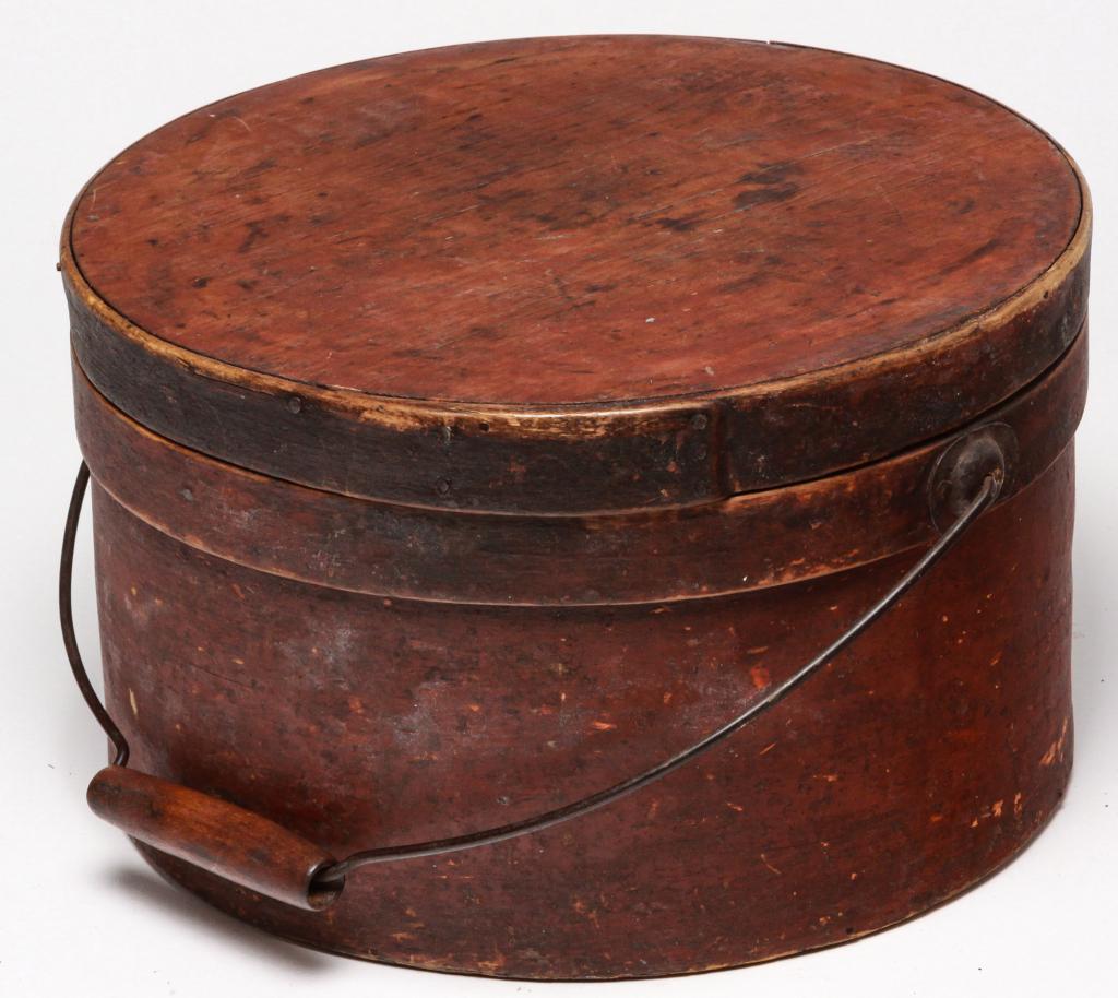 AMERICAN BENTWOOD CARRIER.: Second half 19th century. Round carrier with lapped seams, bentwood band, and bail handle. Original red paint has wear. Some edge loss, glued split in lid. 7"h. 11.75"d.