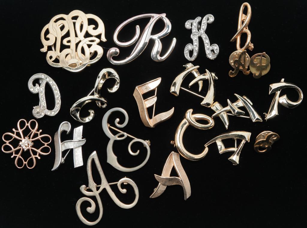 SMALL COLLECTION OF INITIAL PINS.: American, mid-late 20th century. Nineteen pins and one clip with various initials, one with monogram, some embellished with rhinestones. Marked pieces by Trifari, Avon, and BeauJewels.