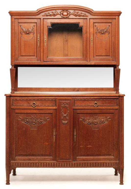 FRENCH BUFFET.: Circa 1900, oak. Arched pediment, floral and foliate carvings, top with center beveled glass door flanked by single panel doors, fluted rounded corners and supported by turned fluted pilasters and bev