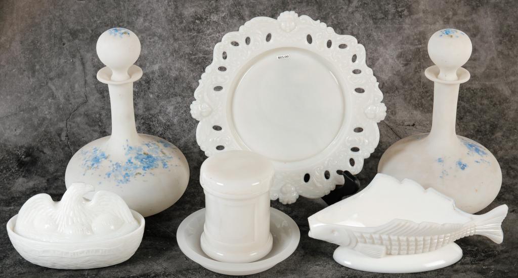 SEVEN PIECES OF MILK GLASS.: Late 19th century. A Spanish American War eagle covered dish, a pair of cologne bottles with blue floral decoration, covered jar, fish shaped dish, shallow bowl and a plate with reticulated edge.