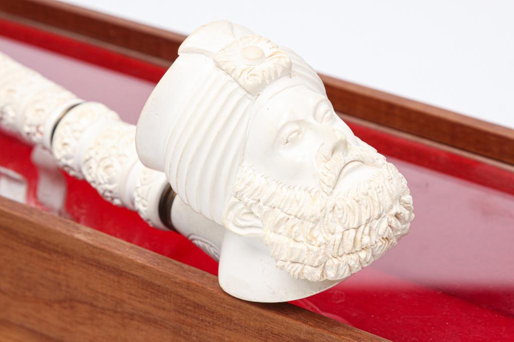 EUROPEAN MEERSCHAUM PIPE.: Early 20th century. Carved four section stem with bakelite lip and a bowl in the form of a man wearing a turban. Lip has small edge flake. 17.25"l. Includes display case.