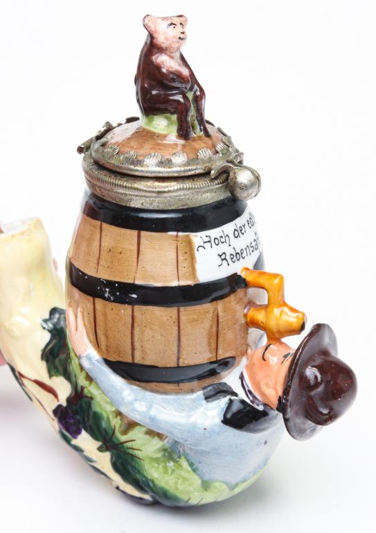 GERMAN FIGURAL PIPE BOWL.: Late 19th-early 20th century. Hand painted porcelain. Man drinking from a keg with an animal finial on the lid. "Hoch der edle Rebensaft". Minor wear, repair at neck. 4"h.