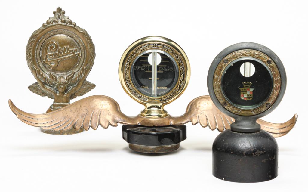 THREE CADILLAC RADIATOR CAPS.: First quarter 20th century. Two Boyce: One thermometer on base, dated 1918, 5.75"h. And other has added wings, 5.5"h. Together with a made-up brass cap, 6.5"h.