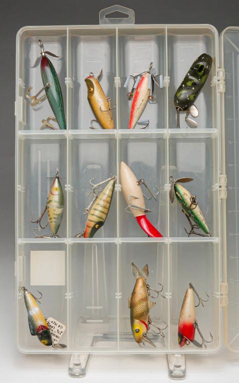 ELEVEN EARLY FISHING LURES INCLUDING SHAKESPEARE.: First half, 20th century. Group of eleven fishing lures. Includes four Shakespeare lures, a SkipJack, and others unmarked. Most are wooden, some with glass eyes. Included is a Shimano clear tackle box