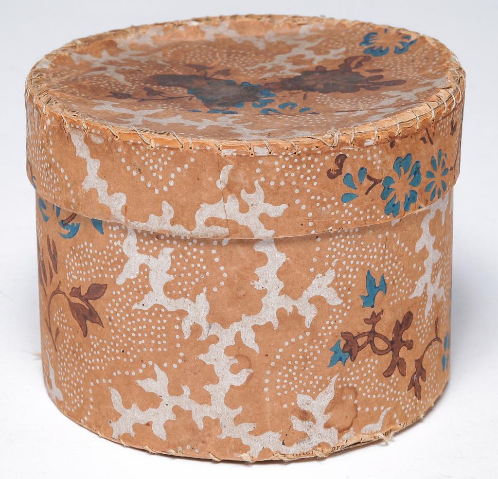 AMERICAN MINIATURE BAND BOX.: Mid 19th century. Round cardboard box covered with block printed wallpaper. Foliage on tan. Newspaper interior and underside dated 1852. Wear and stitched seams.