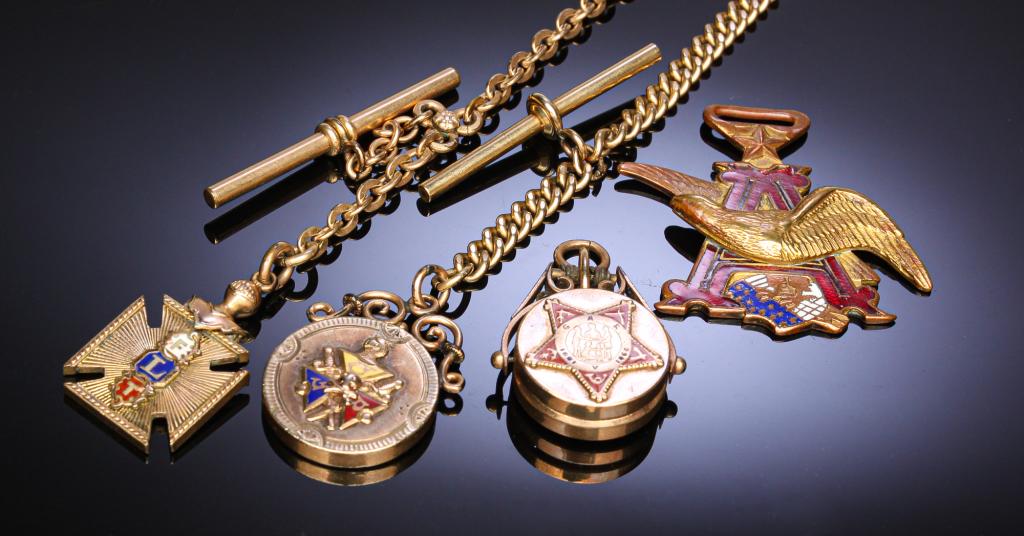 SMALL GROUP OF POCKET WATCH ACCOUTREMENTS.: Second half 19th century. Knights of Pythics charm and flat-link chain, 11"l. Odd Fellows charm and chain, 10.5"l. GAR locket charm with tigers eye back and Anheuser-Busch enameled emblem fob end. PLE