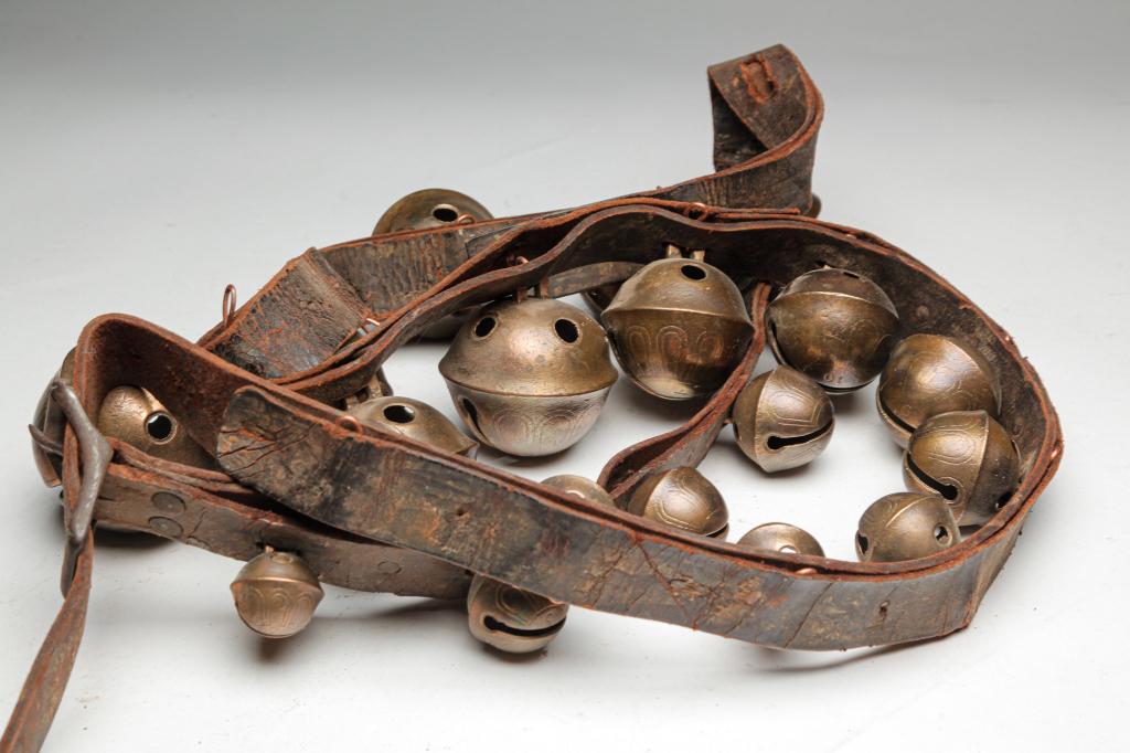 AMERICAN SLEIGH BELLS.: Nineteenth century. Graduated brass sleigh bells attached to leather strap with copper pins. Leather has wea. 40"l.
