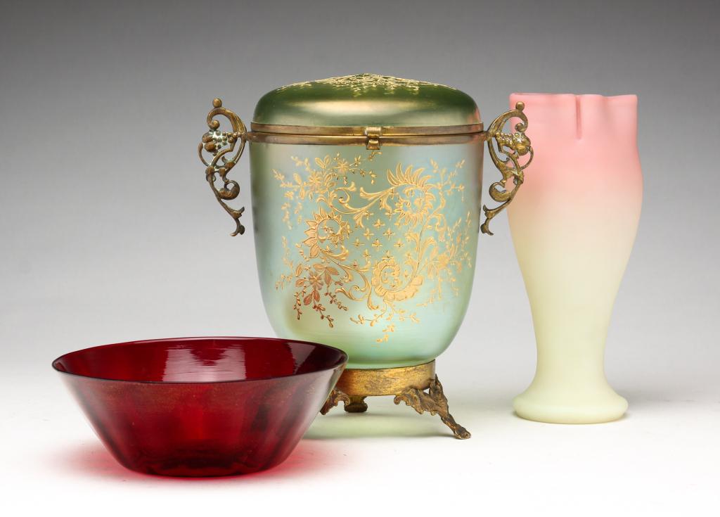 THREE PIECES OF ART GLASS.: American and European, 20th century. Fenton Burmese vase with ruffled edge. 7"h. Red and gold glass bowl. 5.6"w. Green lidded jar with gold painted designs attached to brass stand. 7.25"h.