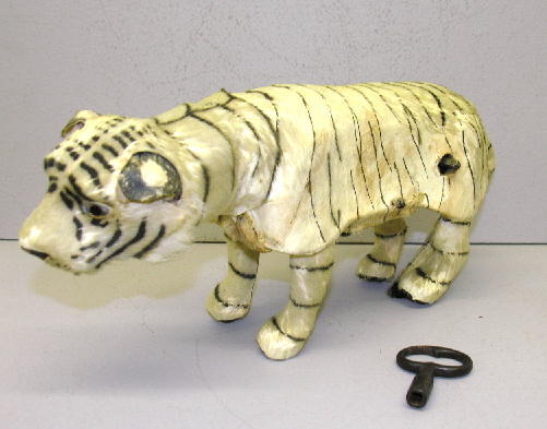 KEY WIND TIGER, 15" PLUS TAIL. Glass eyes, hide co: KEY WIND TIGER, 15" PLUS TAIL. Glass eyes, hide covered with attached ears, painted nose and mouth, original key. When wound the tiger looks to sides, crouches, then leaps. Age wear with some fur miss