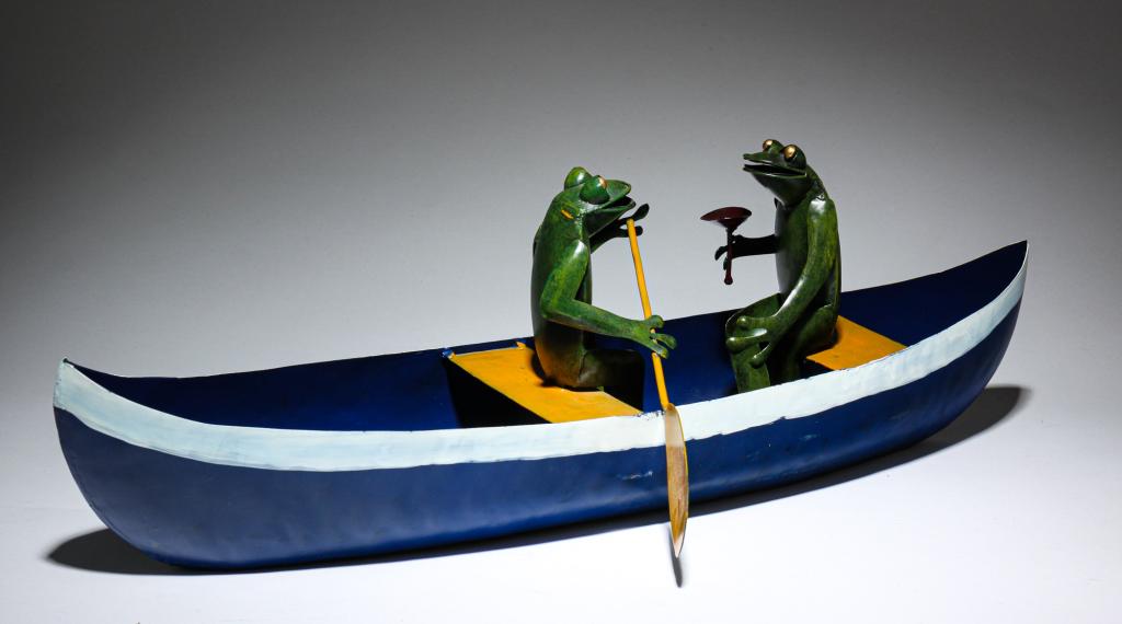 TIN CANOE WITH FROGS.: Twentieth century. Blue canoe with white stripe and yellow seats manned by two frogs, one paddling and one passenger. 8"h.