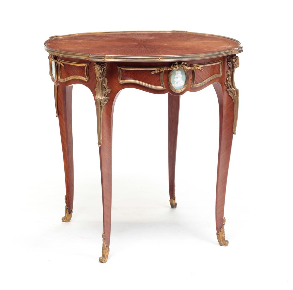 EUROPEAN LOUIS XV STYLE CENTER TABLE.: First quarter 20th century, mahogany figured veneer. Brass ormolu, jasperware oval medallions and shaped legs and apron. Some loose veneer and stains. 29.25"h. 30"dia.