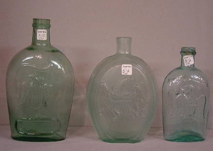 THREE AQUA EAGLE FLASKS. Pictured is a p: THREE AQUA EAGLE FLASKS. Pictured is a pint, GII-118. Blisters. 7 1/4"h.; quart GII - 48, eagle and "Coffin & Hay, Hammonton". Sick. 8"h. And a quart GXI-30. "For Pike's Peak". Wear and some residue.