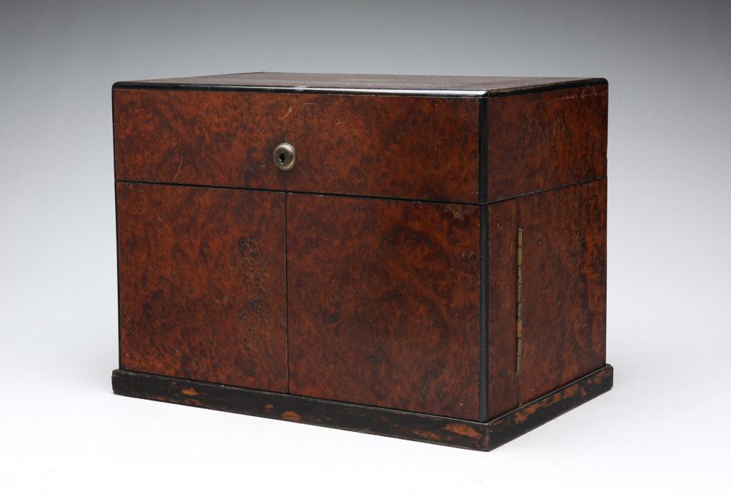 ENGLISH TANTALUS.: Fourth quarter 19th century, burled amboyna, ebony and satinwood. Hinged lid and front doors, interior with three cut glass decanters, missing one stopper and fitted slots for fourteen cordials. Brass
