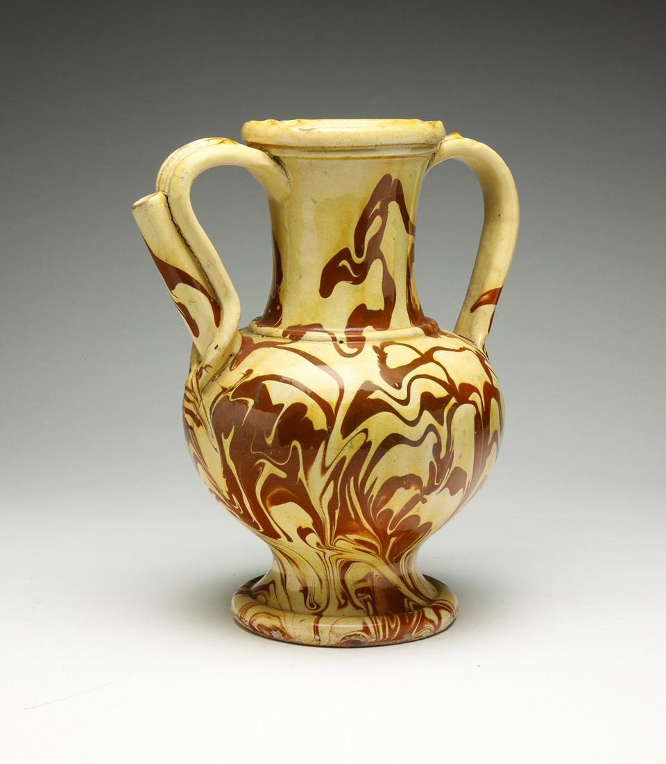 EUROPEAN REDWARE EWER.: First half 19th century. Vase form with hidden spout on handle. Mottled yellow and red glaze. Some wear and edge flakes. 12.5"h.