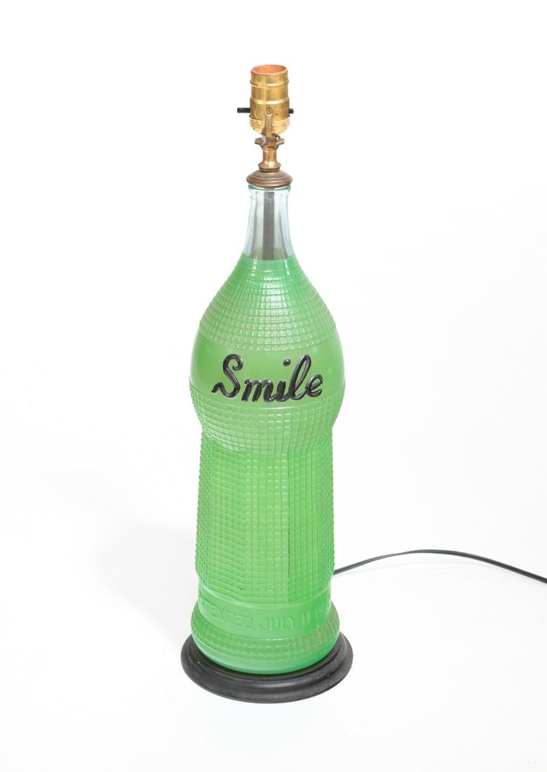AMERICAN "SMILE" SODA ADVERTISING BOTTLE.: Mid 1920's. Green paint with black lettering. Drilled to make a lamp. Some wear to bottle.18"h. 23"h. overall.