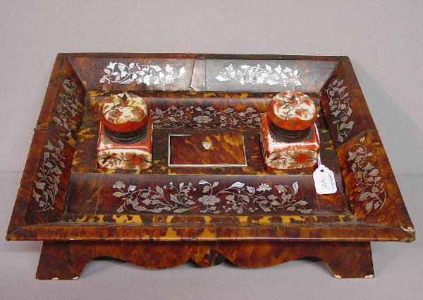 TORTOISE SHELL VENEER DESK SET. Canted g: TORTOISE SHELL VENEER DESK SET. Canted gallery and scrolled apron with floral mother-of-pearl inlay and ivory pads on the feet. Small ivory lined compartment and two porcelain inks with hand painted o