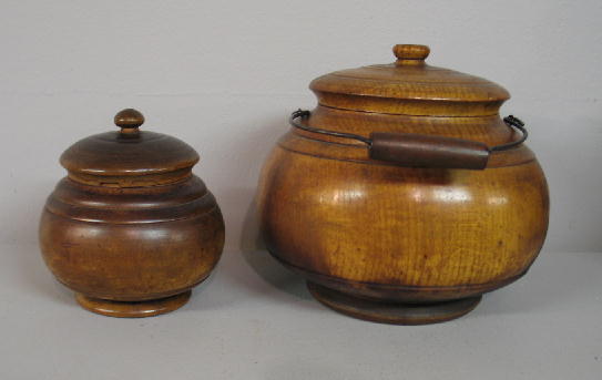 TWO PEASEWARE JARS. Turned wood covered containers: TWO PEASEWARE JARS. Turned wood covered containers with varnish finish and good patina and the larger has a wire bale handle. The larger has age splits and a glued lid, 7 1/4"d. 7"h. The smaller has e