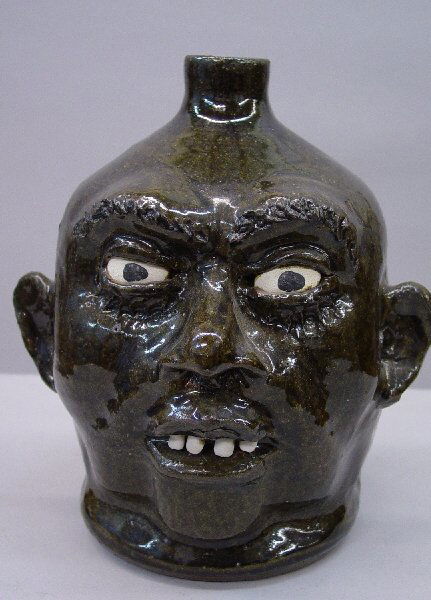 SOUTHERN POTTERY FACE JUG SIGNED "LANIER: SOUTHERN POTTERY FACE JUG SIGNED "LANIER MEADERS, 8-16-78". Dark green glaze with white and black eyes and four pottery teeth. Applied strap handle and ears. 9"h.