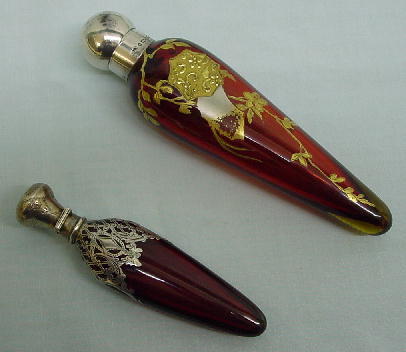 TWO RUBY SPEAR FORM SCENT BOTTLES. One has a ruby i: TWO RUBY SPEAR FORM SCENT BOTTLES. One has a ruby interior encased in light amber glass. Japanesque gilt design has some wear. Silver cap hallmarked for Chester, 1884. 5 3/4"l. Other has silver plate