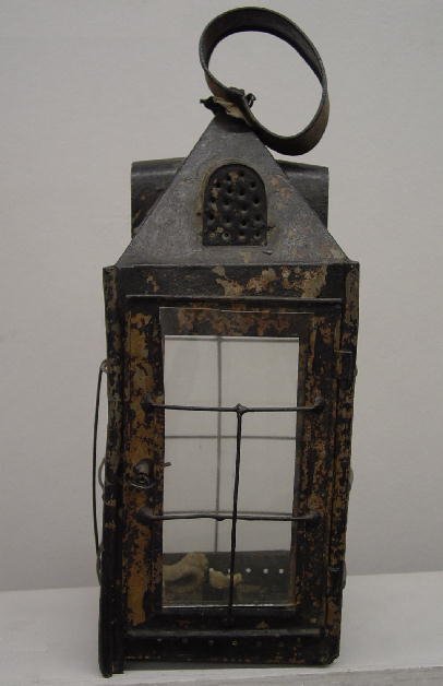 TIN CANDLE LANTERN. Peaked lantern with four vents: TIN CANDLE LANTERN. Peaked lantern with four vents resembling dormer windows and a ring handle. Four panes of replaced glass are protected by wire guards. Door with wire latch. Old worn black paint. 1