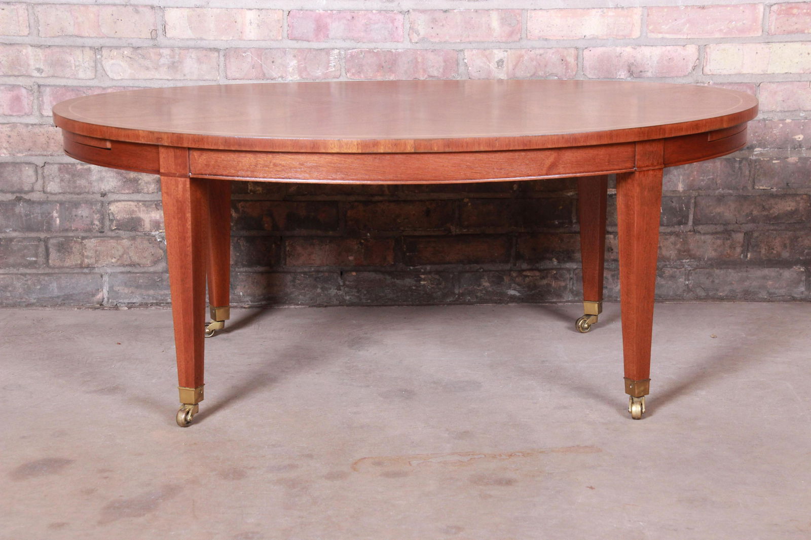 Authentic Baker Furniture Federal Mahogany Oval Coffee: An exceptional Federal style coffee table with extension trays By Baker Furniture USA Circa 1980s Book-matched mahogany with brass accents and casters. Measures: 41.75"W x 27.75"D x 17"H. Extends to 6