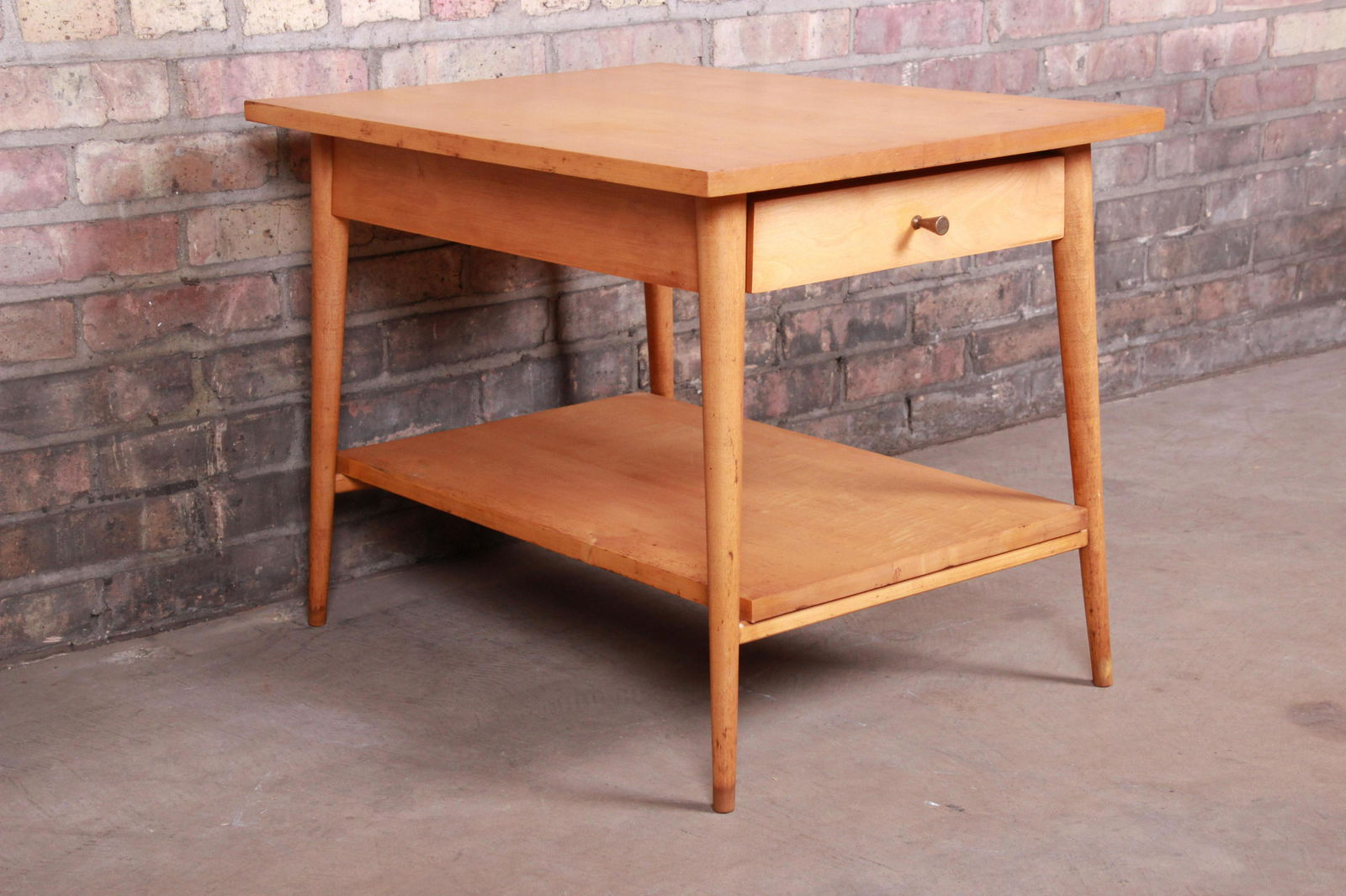 Authentic Paul McCobb Planner Group Mid-Century Modern: A sleek and stylish mid-century modern nightstand or side table By Paul McCobb for Winchendon Furniture "Planner Group" USA 1950s Solid maple with original brass drawer pull. Measures: 19.25"W x 26.38