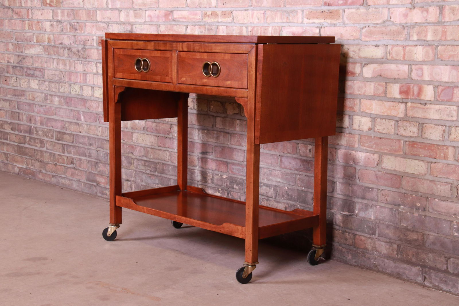 Authentic Michael Taylor for Baker Furniture Far East: An exceptional mid-century modern extension bar cart By Michael Taylor for Baker Furniture "Far East Collection" USA Circa 1960s Book-matched walnut with iconic brass interlocking ring pulls and origi
