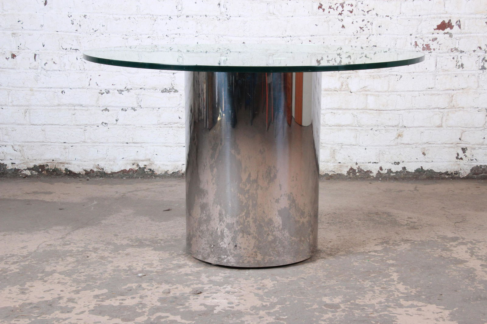 Brueton Mid-Century Modern Polished Steel and Glass: A sleek and stylish mid-century modern drum base pedestal dining or center table By Brueton USA Circa 1970s Polished steel base + thick glass table top Measures: 48"W x 48"D x 30"H. Glass top 0.75" th