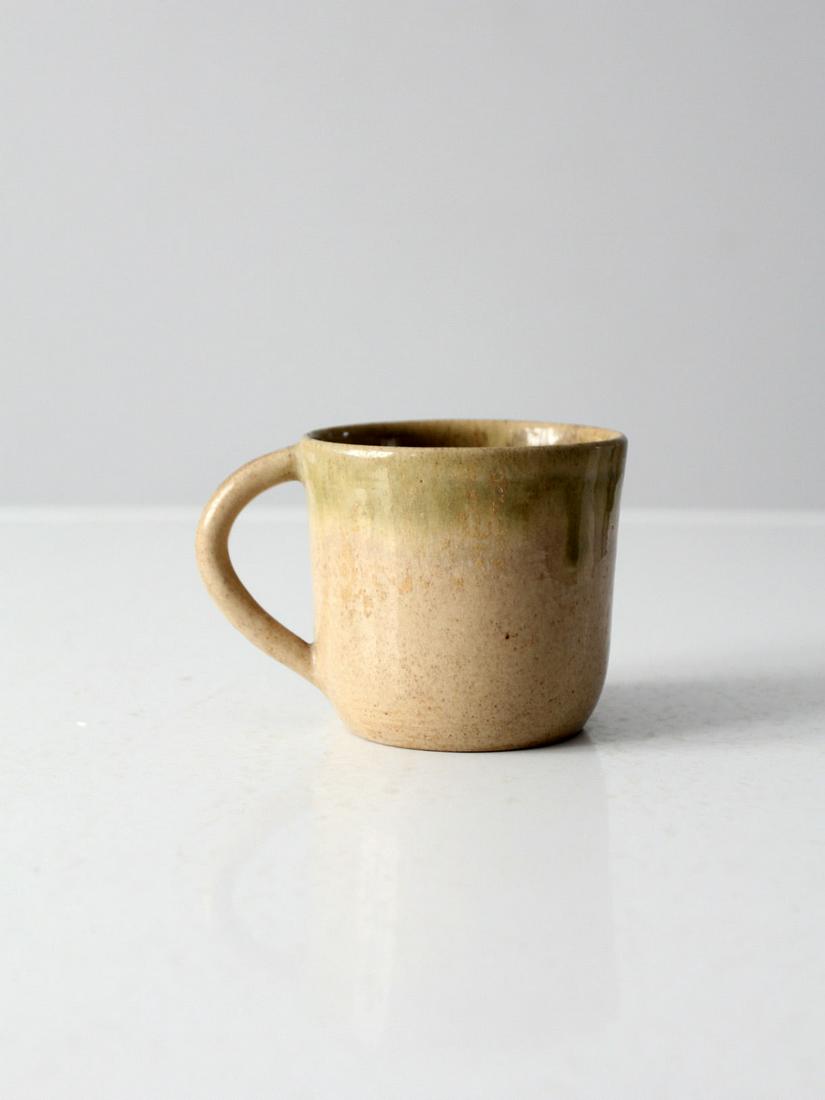 Vintage Eugene Deutch Pottery Mug: Vintage Eugene Deutch Pottery Mug This is a Eugene Deutch pottery mug circa 1950s. The hand-crafted art studio mug features a ecru glaze with pale green accents. Width 5 inch 12.7 cm Depth 3.5 inch 8.