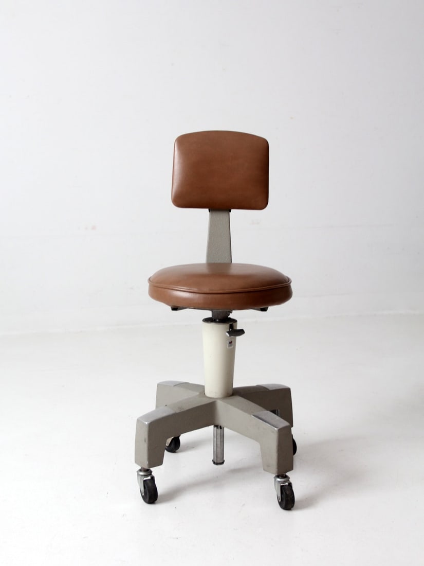 Vintage American Optical Industrial Rolling Stool: Vintage American Optical Industrial Rolling Stool This is a mid 20th century vintage optometrist chair by the American Optical Company. The adjustable rotating stool features a brown vinyl upholstered