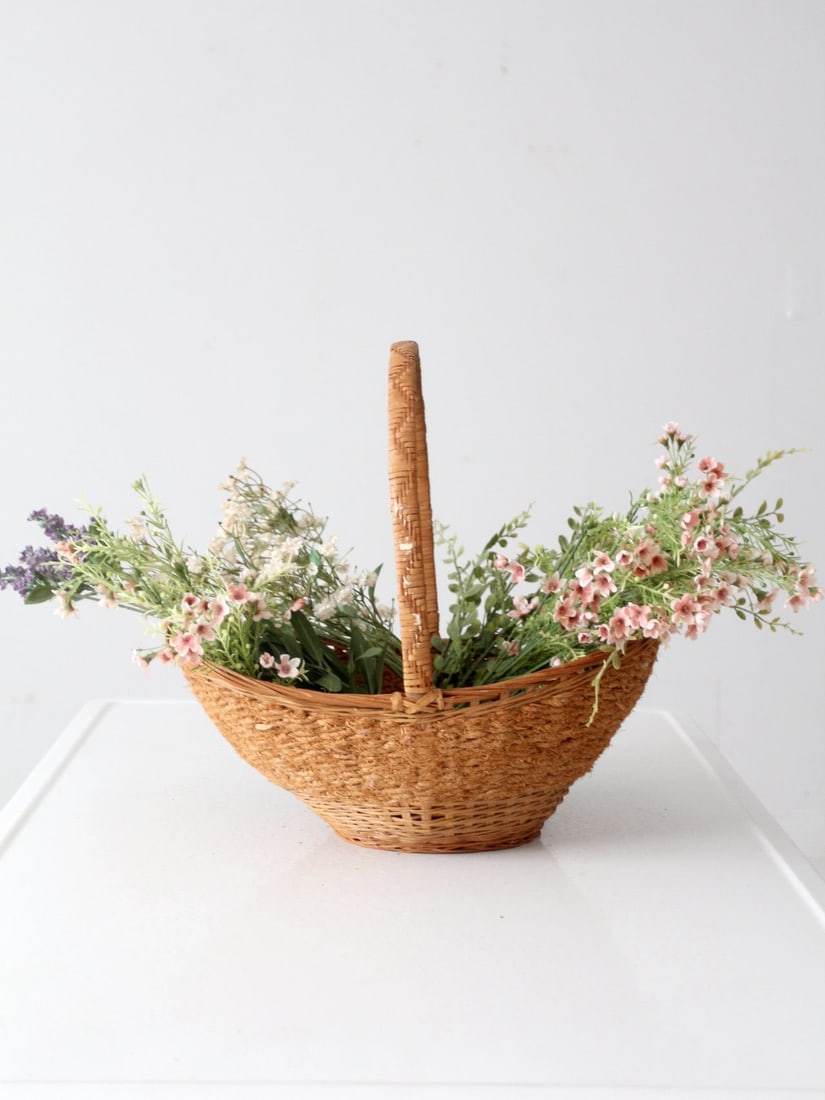 Vintage Wicker Basket: Vintage Wicker Basket Add a farmhouse vintage touch to your home with this woven wicker basket! With its box woven handle its perfect for filling with freshly-picked flowers from the garden or for tid