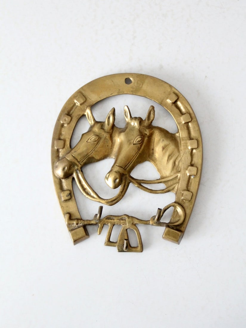 Vintage Brass Horse Wall Hook Rack: Vintage Brass Horse Wall Hook Rack This is a vintage brass equestrian wall hanging with hooks. Two horses look out from a horseshoe frame to shape the wall decor. Two small hooks sit at the base to ha