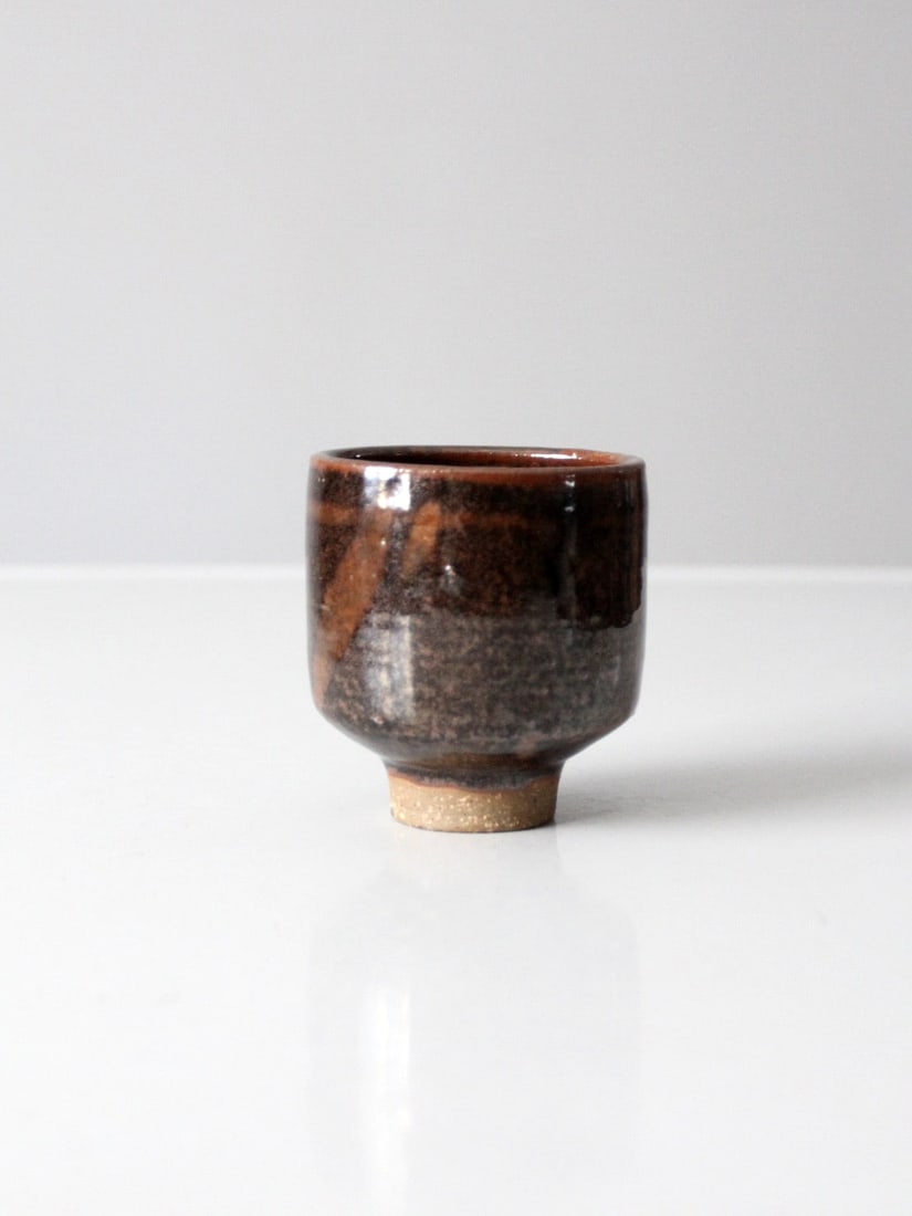 Vintage Studio Pottery Japanese Tea Cup: Vintage Studio Pottery Japanese Tea Cup This is a vintage studio pottery tea cup. The hand-crafted Japanese style tea cup features a russet accented dark brown glaze with pedestal base. Height 3.25 in