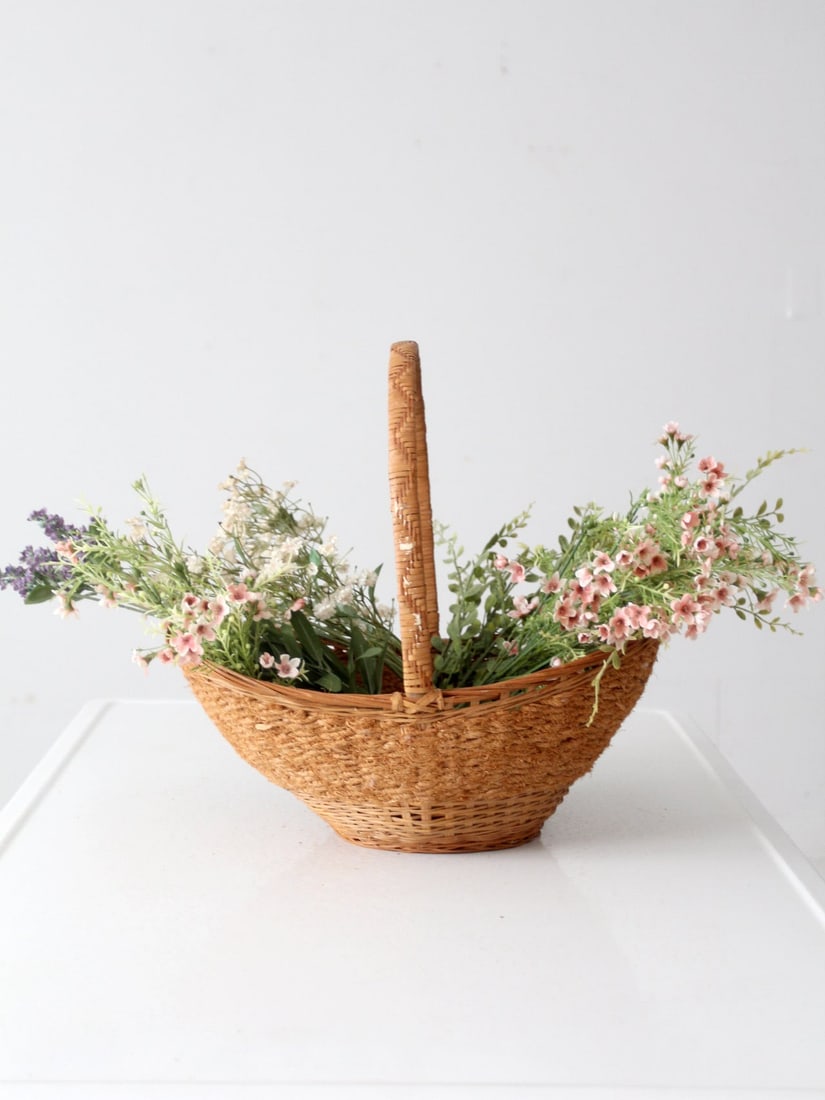 Vintage Wicker Basket: Vintage Wicker Basket Add a farmhouse vintage touch to your home with this woven wicker basket! With its box woven handle its perfect for filling with freshly-picked flowers from the garden or for tid