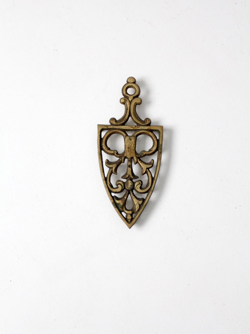 Vintage Brass Trivet: Vintage Brass Trivet A vintage brass trivet. It features a twining vines pattern and small brass feet. There is a hole at the top of the trivet handle for hanging. A wonderful addition to a kitchen. L