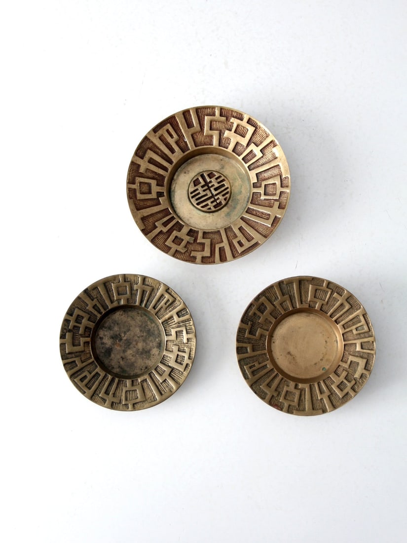 Mid Century Brass Decorative Plates Trio: Enhance your decor with this set of three mid-century brass decorative plates. Featuring brutalist design elements, these pre-owned plates are perfect for wall display with added wire hangers. Ideal f