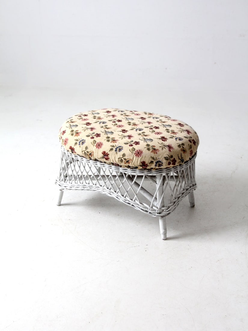 Vintage Oval Wicker Ottoman with Cream Floral Upholstery: Vintage Oval Wicker Ottoman with Cream Floral Upholstery This vintage wicker ottoman showcases a charming oval design with a white wicker frame and cream floral upholstery. Its open weave base adds a 