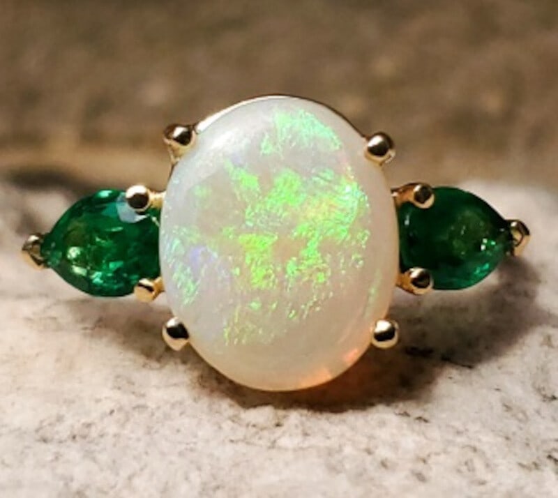 Stunning 18k Yellow Gold Opal Emerald Ring 1.76ct Size 9.25 GIA Certified: Stunning 18k Yellow Gold Opal Emerald Ring 1.76ct Size 9.25 GIA Certified This exquisite 18k yellow gold ring showcases a stunning 1.76ct genuine natural opal surrounded by two fine quality emeralds. 