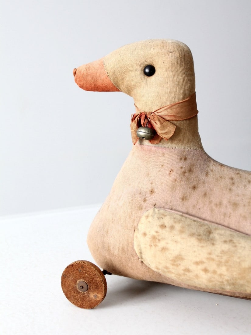 Vintage Early 20th Century Fabric Toy Duck on Wheels: Vintage Early 20th Century Fabric Toy Duck on Wheels This charming antique toy duck on wheels dates back to the early 20th century. Crafted from pink and beige fabric, it features delightful bead eyes