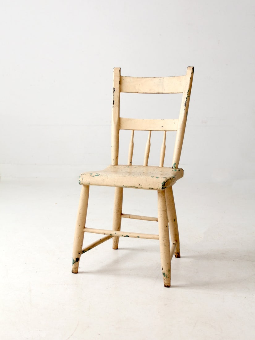 Rustic Antique Spindle Back Chair with Aged Cream Finish: Rustic Antique Spindle Back Chair with Aged Cream Finish This antique primitive chair showcases a classic spindle-back design complemented by a sturdy plank seat. Finished in aged cream paint with hin