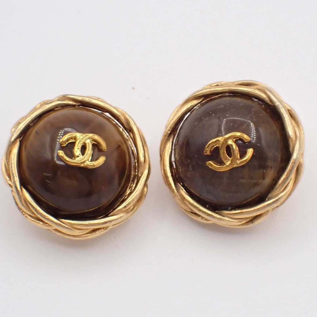 Brown Clip-On Earrings with CC Motif by Chanel: Brown Clip-On Earrings with CC Motif by Chanel These pre-owned Chanel CC Button clip-on earrings feature a brown finish and are designed for women. They are in very good condition, showing minor scuff