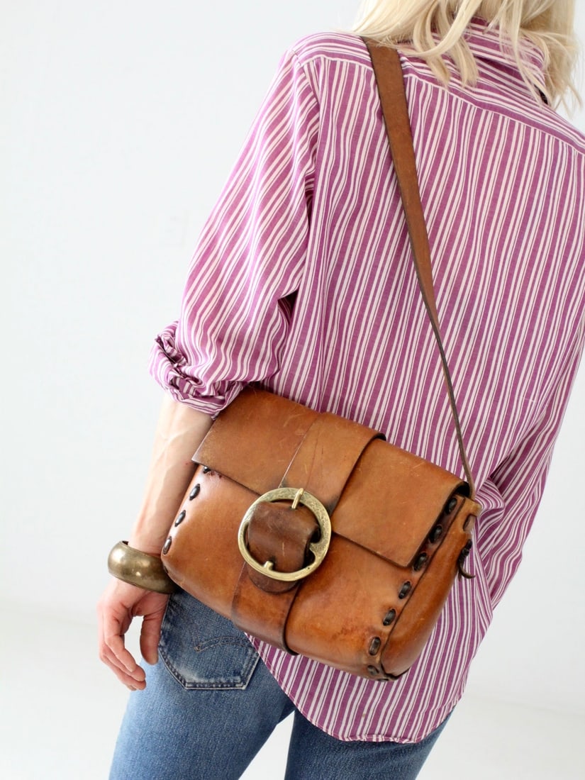 1960s Vintage Hippie Shoulder Bag in Saddle Brown Leather: 1960s Vintage Hippie Shoulder Bag in Saddle Brown Leather Discover the essence of the 1960s with this vintage hippie bag, expertly hand-crafted from thick saddle brown leather. This shoulder bag featu