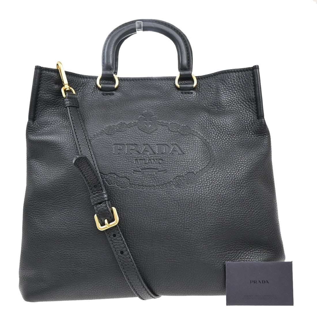 Convertible Black Tote with Embossed Logo by Prada: Convertible Black Tote with Embossed Logo by Prada This pre-owned Prada Embossed Logo Convertible Open Tote is a stylish and practical accessory. It features a black exterior with the Prada embossed l