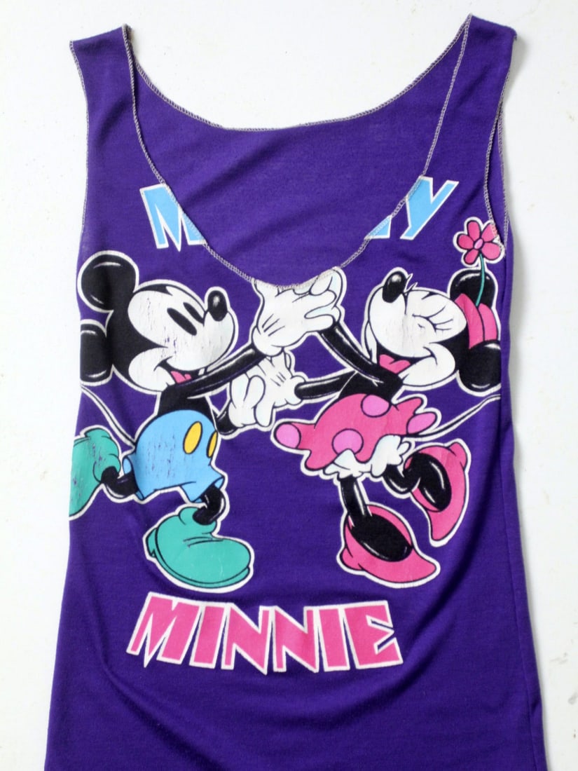 1980s Reworked Purple Tank Featuring Dancing Mickey and Minnie Mouse: 1980s Reworked Purple Tank Featuring Dancing Mickey and Minnie Mouse This vintage 1980s Mickey and Minnie Mouse tank top features a bold purple graphic on the front, showcasing Mickey and Minnie danci