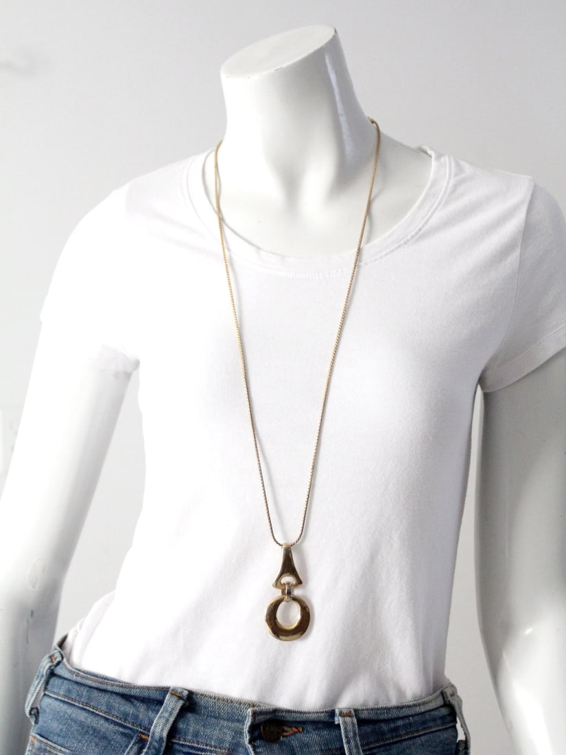 Vintage Gold Tone Long Pendant Necklace with Geometric Hoop: Vintage Gold Tone Long Pendant Necklace with Geometric Hoop Discover this vintage long pendant necklace that showcases a stunning gold tone finish. The piece features a long linked chain, measuring 34
