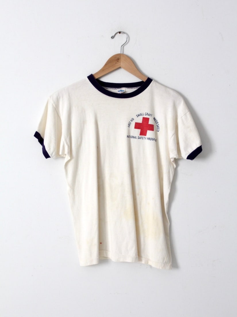 1980s Champion Ringer Tee First Aid Water Safety T-Shirt: 1980s Champion Ringer Tee First Aid Water Safety T-Shirt Step back in time with this vintage 1980s Champion Graphic Ringer Tee featuring a First Aid Water Safety design. Made from 100% cotton, this wh